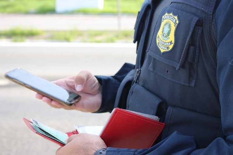 Imagem de um caminhão parado e policiais rodoviários federais fazendo a verificação dos documentos e detendo o motorista pelo uso de documento falso em Seabra